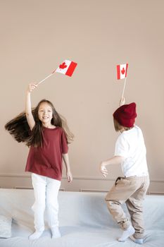 Two children joyfully wave Canadian flags indoors, celebrating Canada Day.