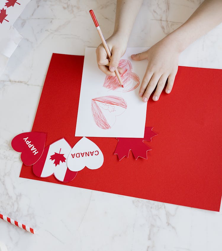 Hands Of A Child Drawing Red Hearts On Paper