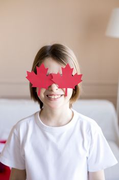 Smiling child with maple leaf glasses celebrating Canada Day indoors.