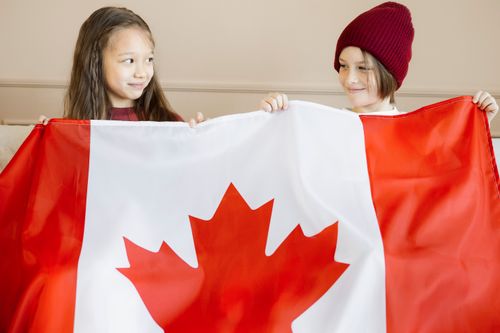 Free Two children joyfully holding the Canadian flag indoors, celebrating national pride. Stock Photo