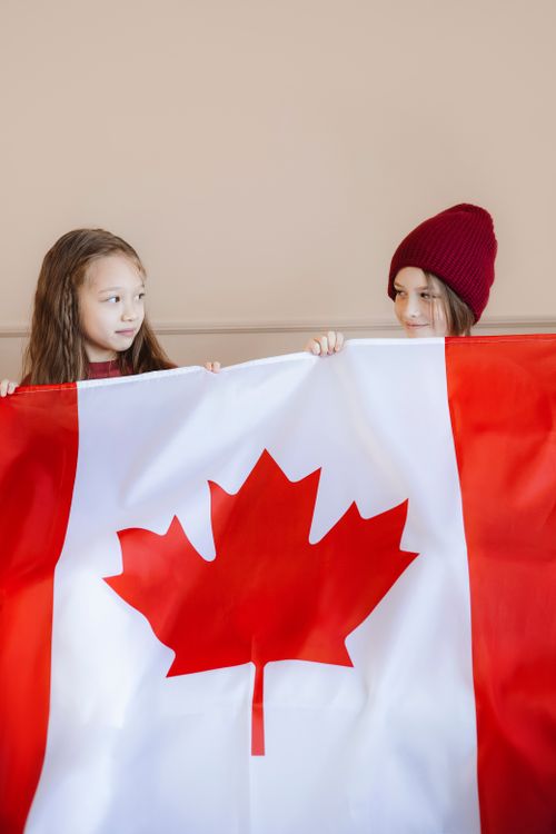 Free Two children holding a Canadian flag indoors, showcasing patriotism and happiness. Stock Photo
