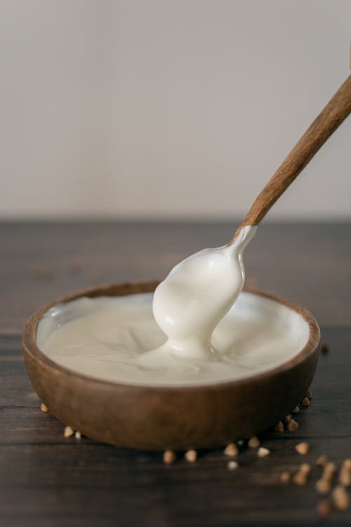 From above of anonymous person stirring sour cream with spoon in wooden bowl placed on table against blurred background