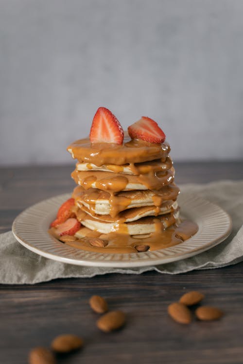 Free Yummy soft freshly prepared pancakes topped with caramel sauce and decorated with rip strawberries and almonds Stock Photo