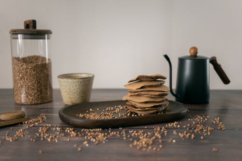 Free Yummy buckwheat chocolate stuff pancakes served on wooden plate with glass jar of grains and kettle with cup Stock Photo