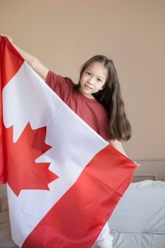 Portrait of a young girl proudly holding a Canadian flag inside a neutral-toned room.