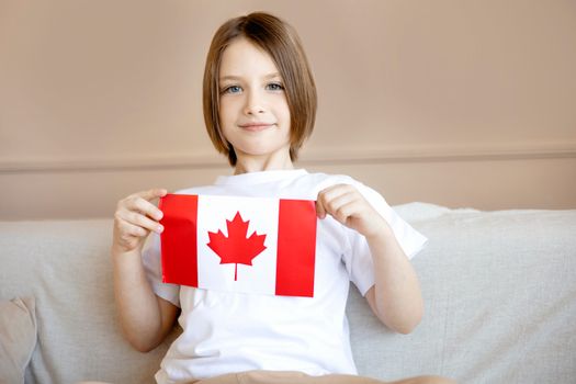A young boy proudly holding a Canadian flag while sitting indoors, displaying patriotism.