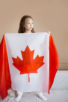 A young girl stands indoors holding a Canadian flag, symbolizing patriotism and national pride.