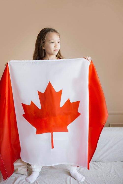 Free A young girl stands indoors holding a Canadian flag, symbolizing patriotism and national pride. Stock Photo