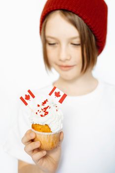 Young girl with red beanie admires cupcake decorated with Canadian flags, embracing national pride.