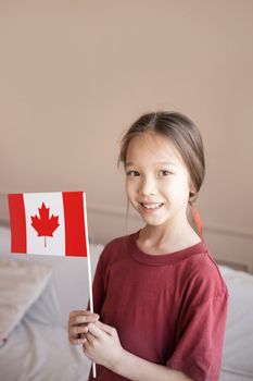 Portrait of a smiling young girl holding a Canadian flag indoors, reflecting Canadian pride.