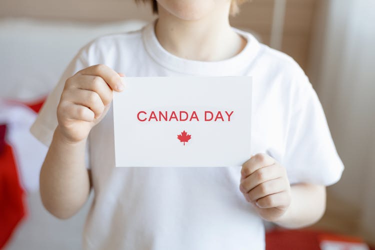 A Child Holding A White Paper With Canada Day Message