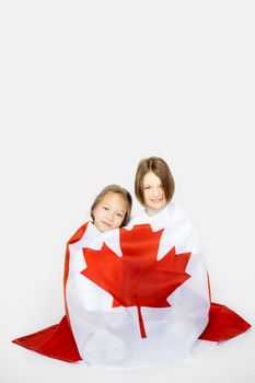 Two smiling kids wrapped in a Canadian flag, symbolizing national pride and unity.