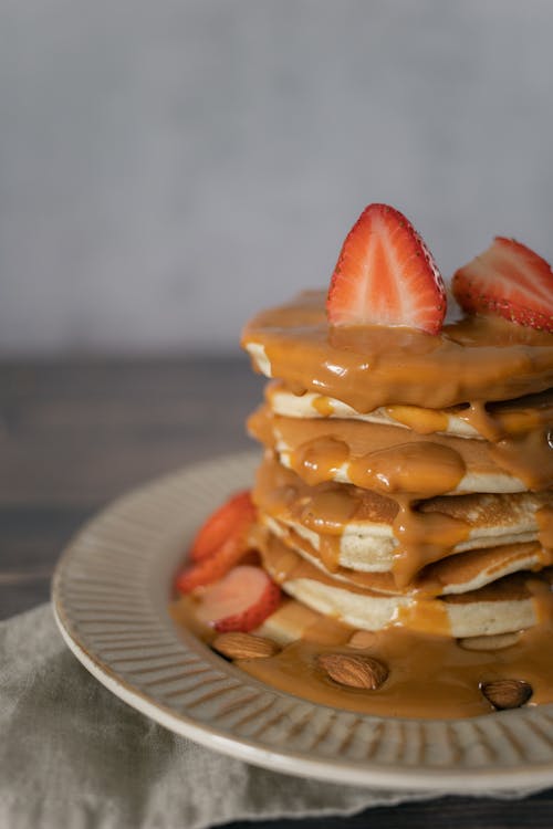 Free Heap of tasty pancakes topped with cut strawberries and sweet caramel served on white plate on table in light room Stock Photo