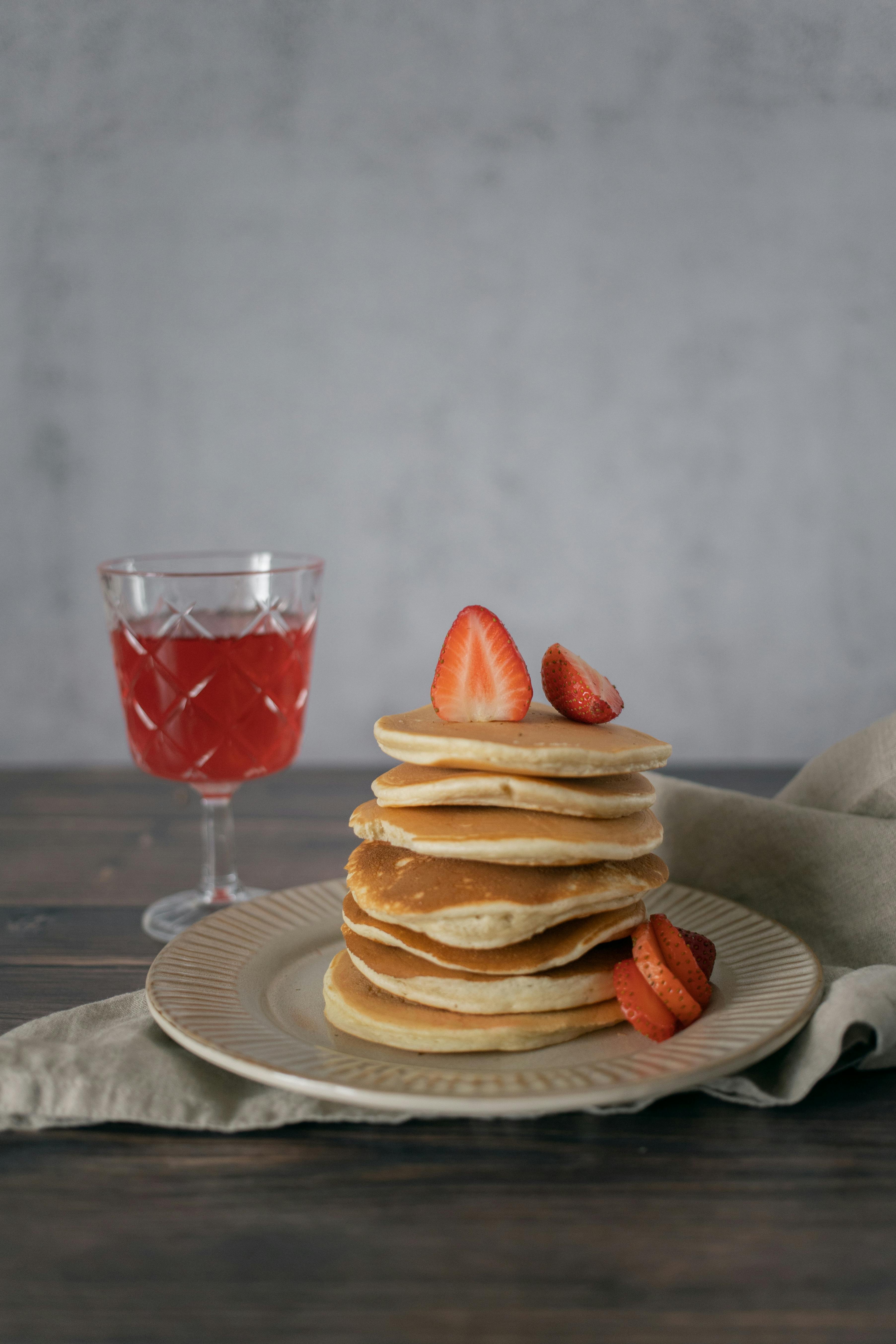 A tempting stack of pancakes with fresh strawberries and a refreshing drink served on a rustic table.