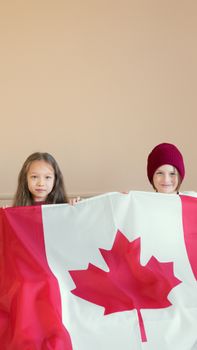 Two children proudly holding a Canadian flag indoors, expressing patriotism.