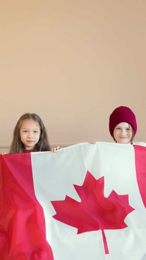 Free Two children proudly holding a Canadian flag indoors, expressing patriotism. Stock Photo