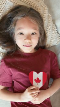 Adorable child holds a heart-shaped Canadian flag emblem, showcasing patriotism with innocence and joy.