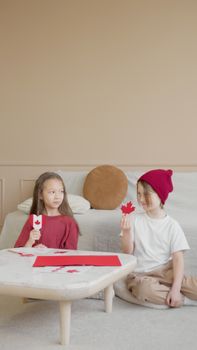 Two children creating Canadian-themed crafts, sitting indoors and enjoying a festive atmosphere.