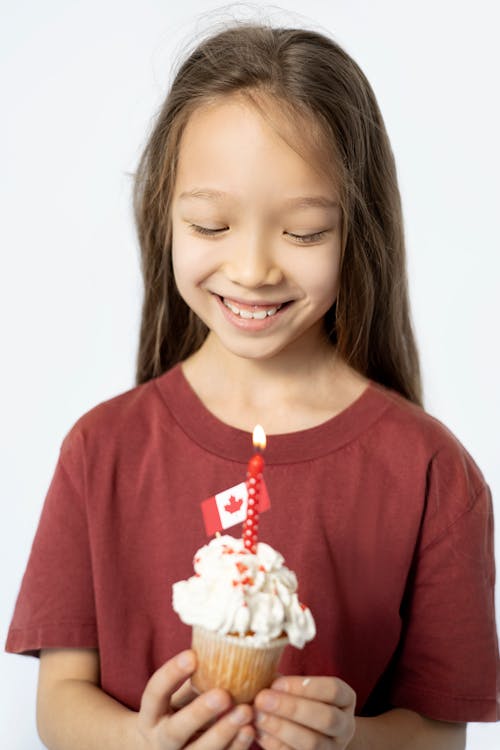 A Girl Holding a Cupcake with Candle and Mini Canada Flag on Top