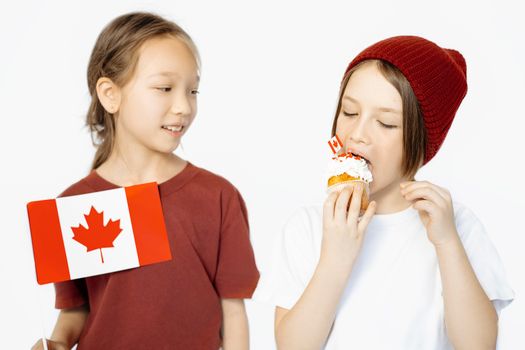 Two kids joyfully celebrate Canada Day with a flag and festive cupcake.
