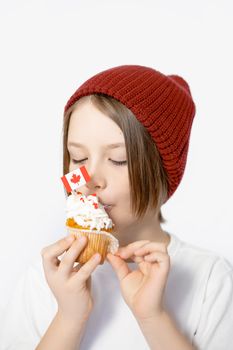 A child wearing a red knit cap enjoys a cupcake with a Canadian flag decoration on a white background.