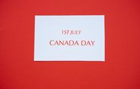 A white card with red text displaying '1st July Canada Day' on a red background.