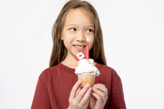 A smiling girl holds a cupcake with a Canadian flag and candle, symbolizing celebration.