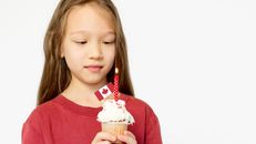 Girl holding a decorated cupcake with Canadian flag and candle on Canada Day.