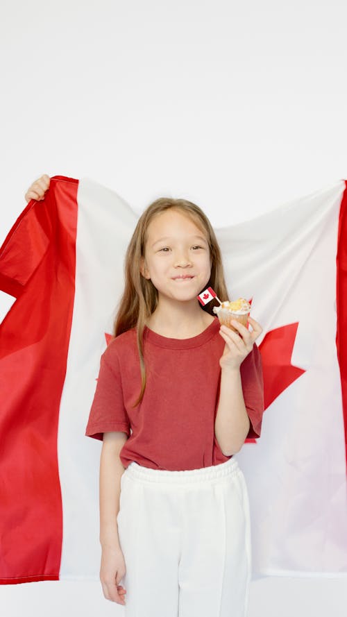 Girl Standing in front of a Canadian Flag while Holding a Cupcake