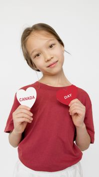 A girl wearing a red t-shirt holds heart-shaped Canada Day symbols.