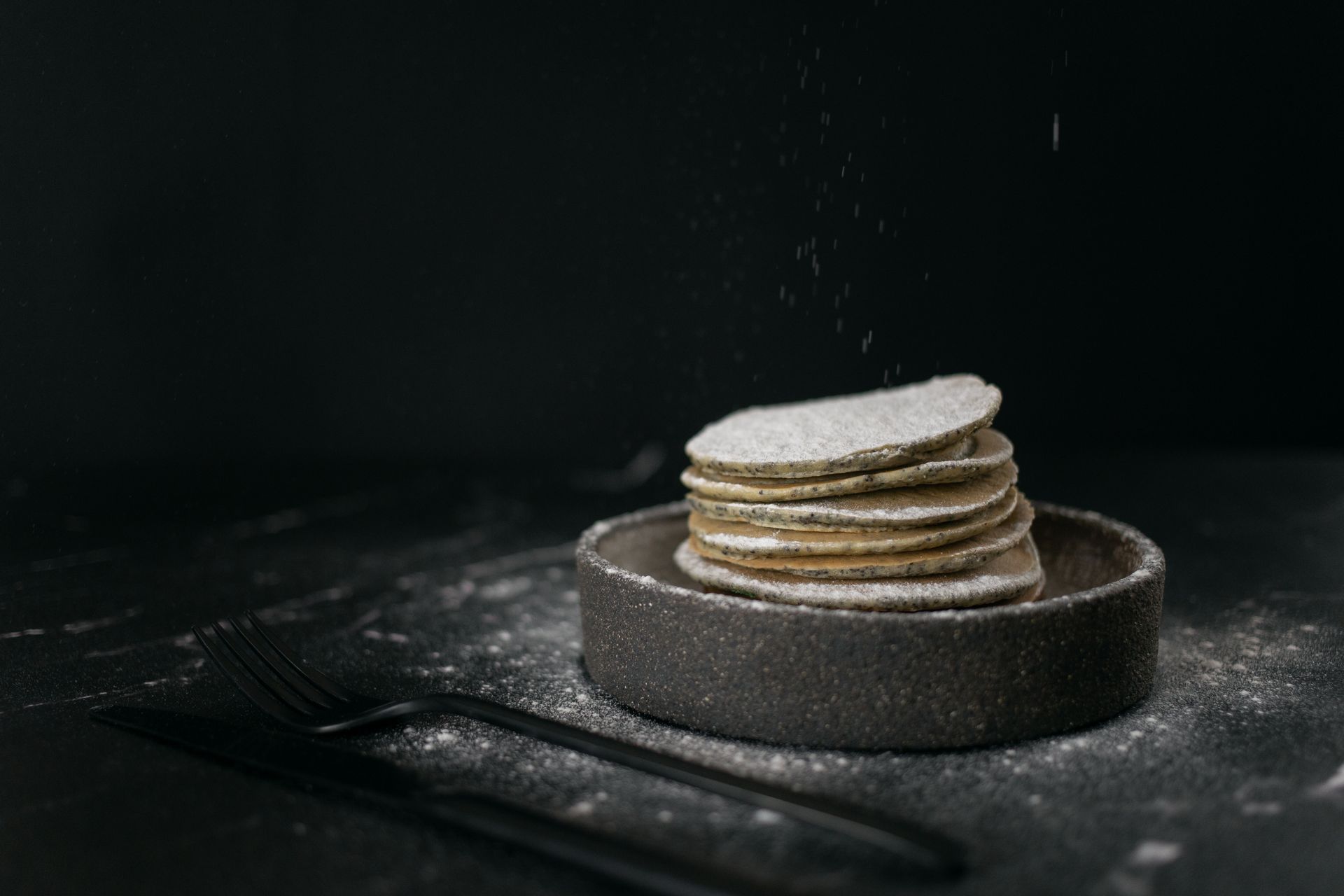 Delicious sweet pancakes placed in baking dish near metal fork and knife on table on black background