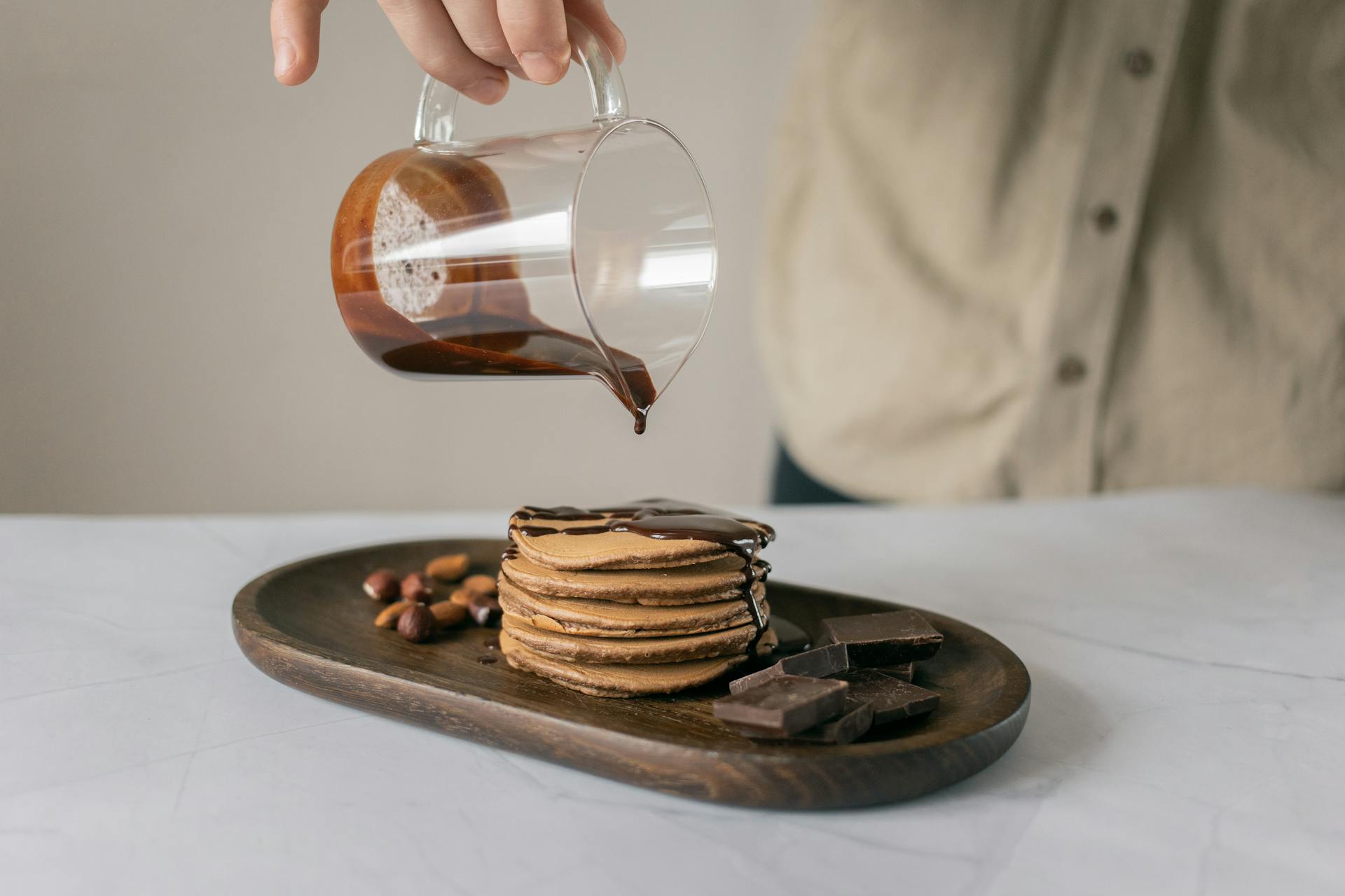 Person Pouring Chocolate Syrup on Brown Pancake