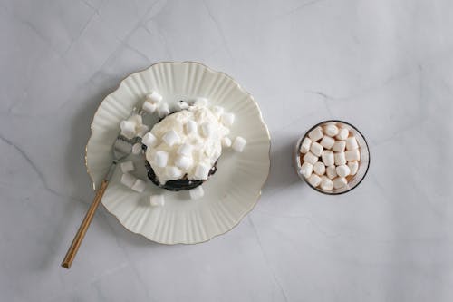 Top view of plate and fork with delicate white marshmallow and chocolate topping near cocoa
