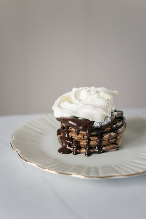 Appetizing sweet chocolate pancake with cream topping placed on plate on white table