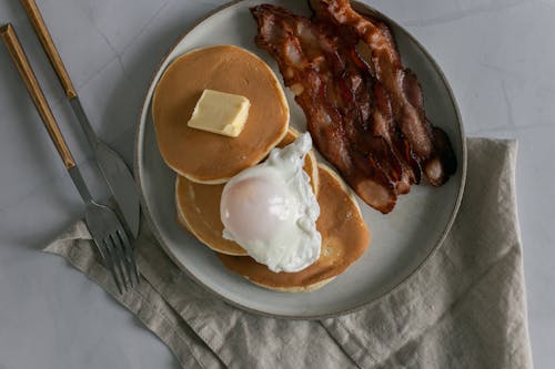 Plate with pancakes with butter near roasted bacon and poached egg