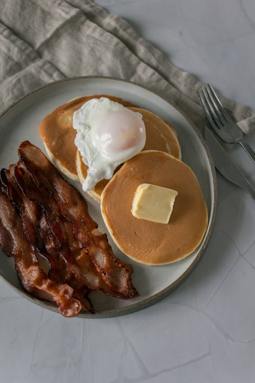 Pancakes near fried bacon slices and poached egg on plate