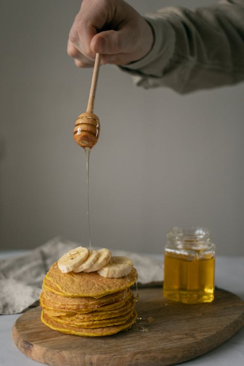 Free Faceless person pouring honey on pancakes with bananas on board Stock Photo