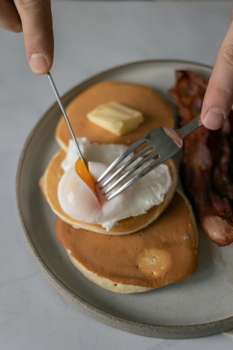 Faceless Person Cutting Poached Egg On Pancakes On Plate