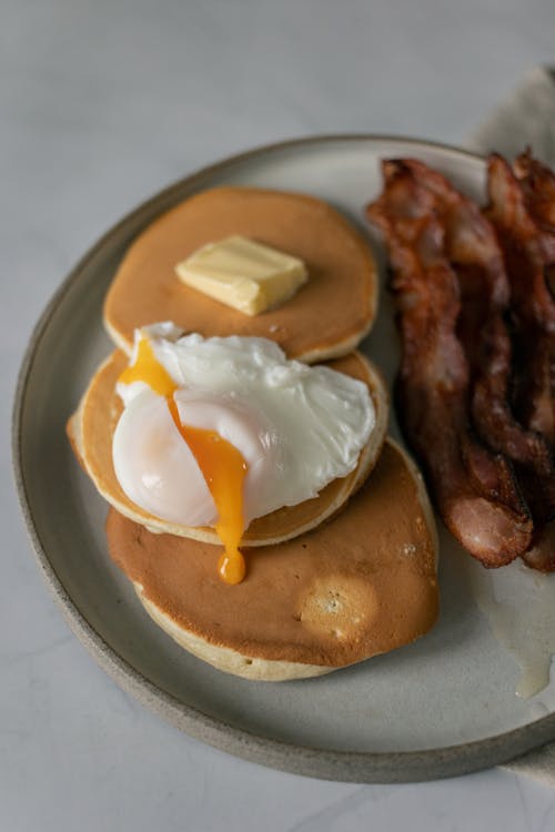 Pancakes near fried bacon slices and poached egg on plate