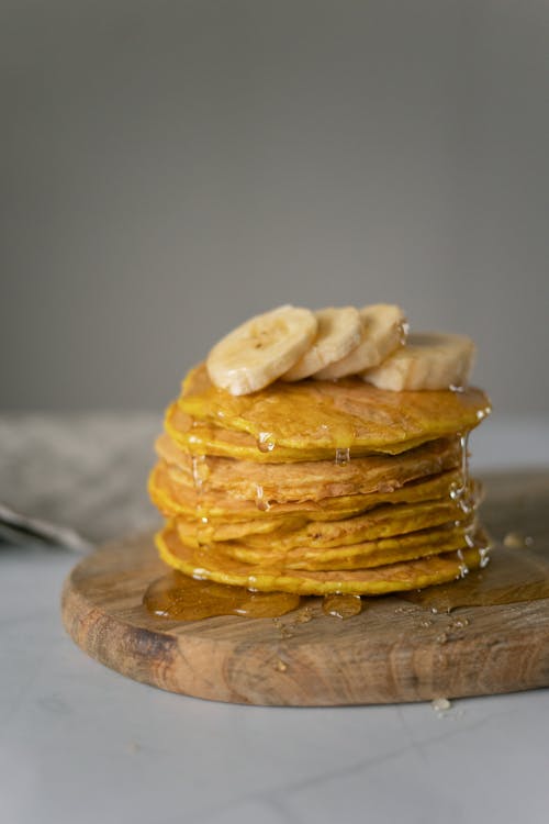 Pancakes with honey and bananas on chopping board on table
