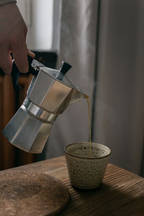Free Close-up of coffee pouring into a ceramic cup from a moka pot on a wooden table. Stock Photo