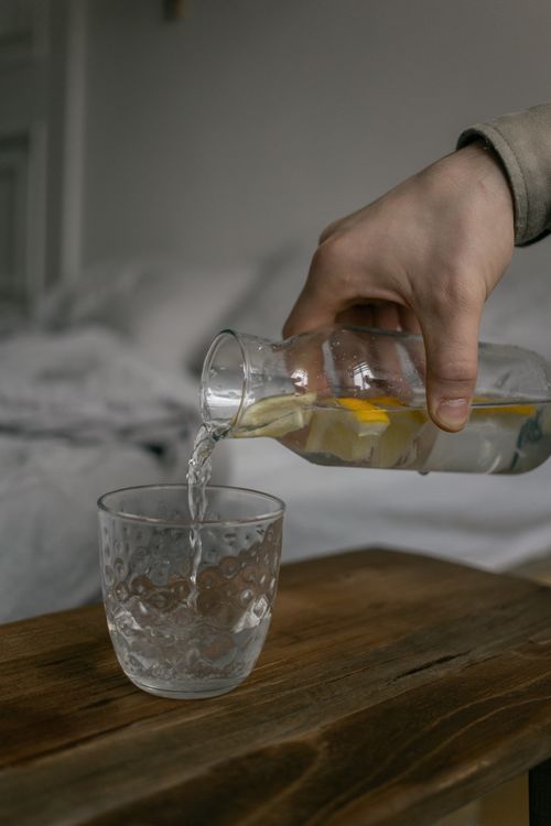 Free Close-up of a hand pouring lemon-infused water from a glass bottle into a glass on a wooden table. Stock Photo