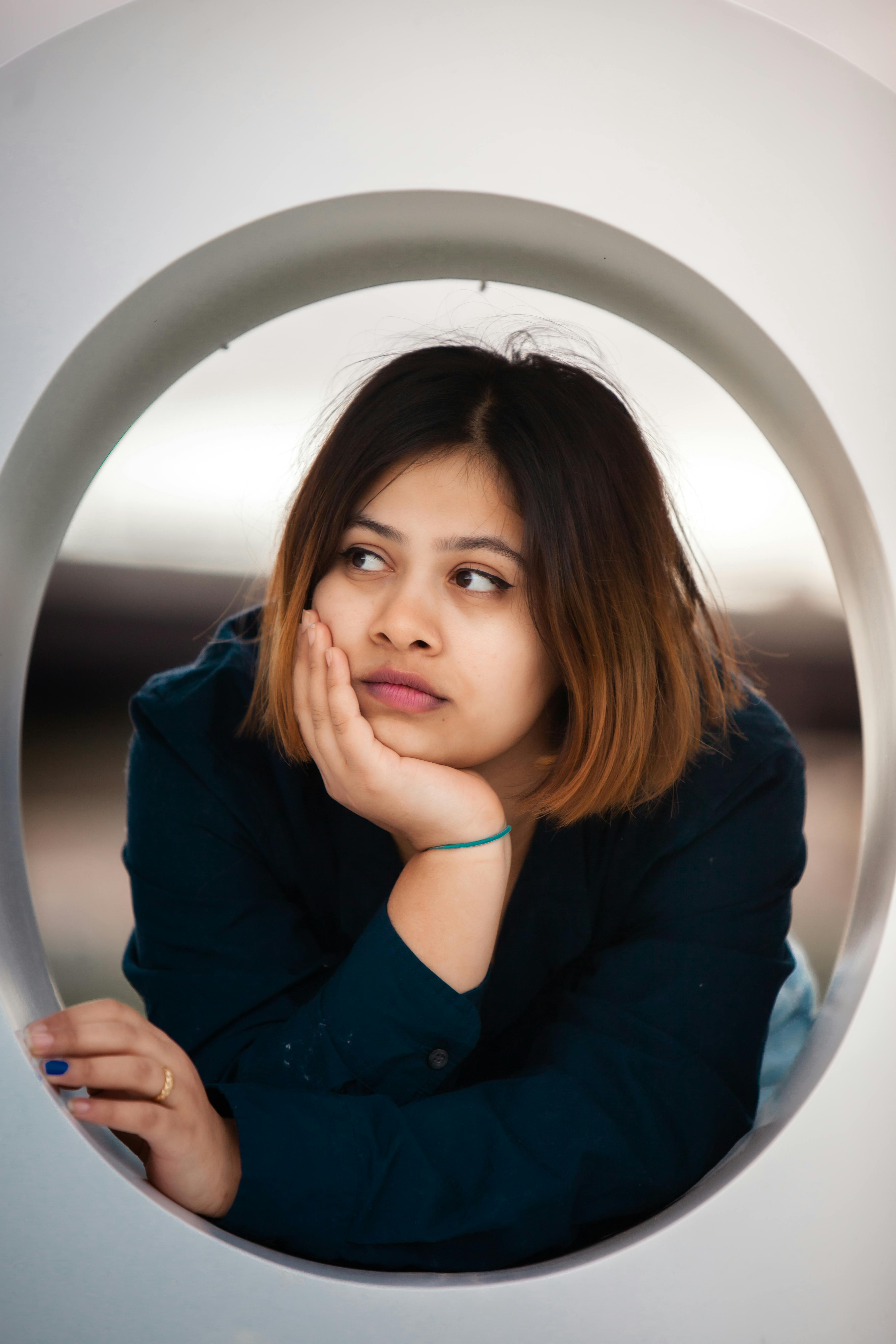 A woman with short hair rests her chin on her hand, gazing thoughtfully.