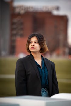 Stylish young woman in a black blazer posing with serious expression in an urban outdoor environment.