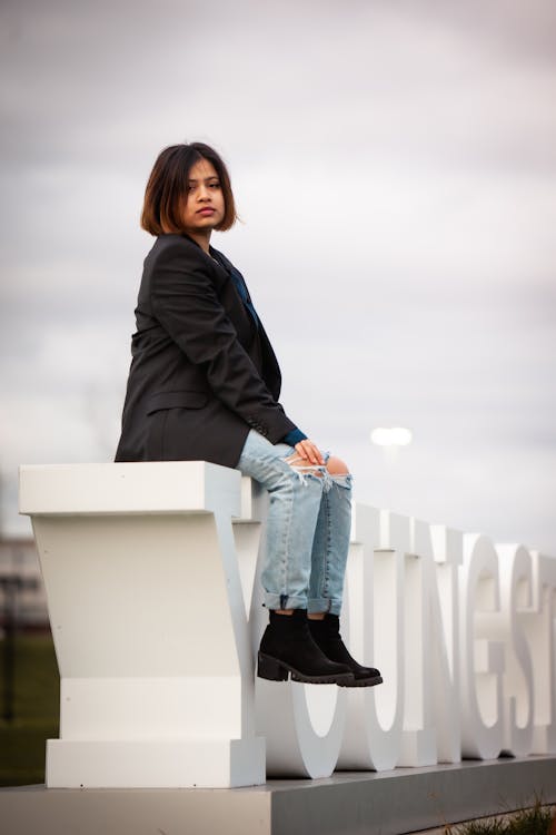 Free Woman in Black Blazer Sitting on Standing Concrete Signage Stock Photo