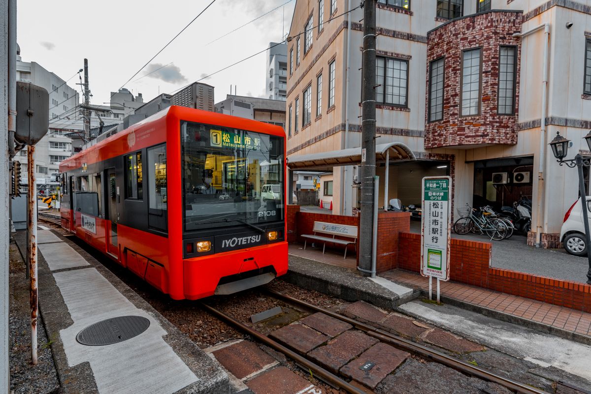 A red Iyotetsu tram at a stop in Matsuyama