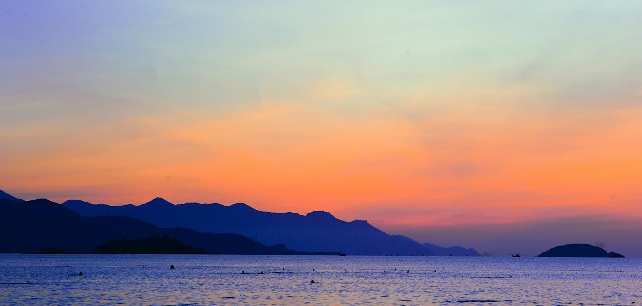 橙色日落期間海洋旁邊山的輪廓