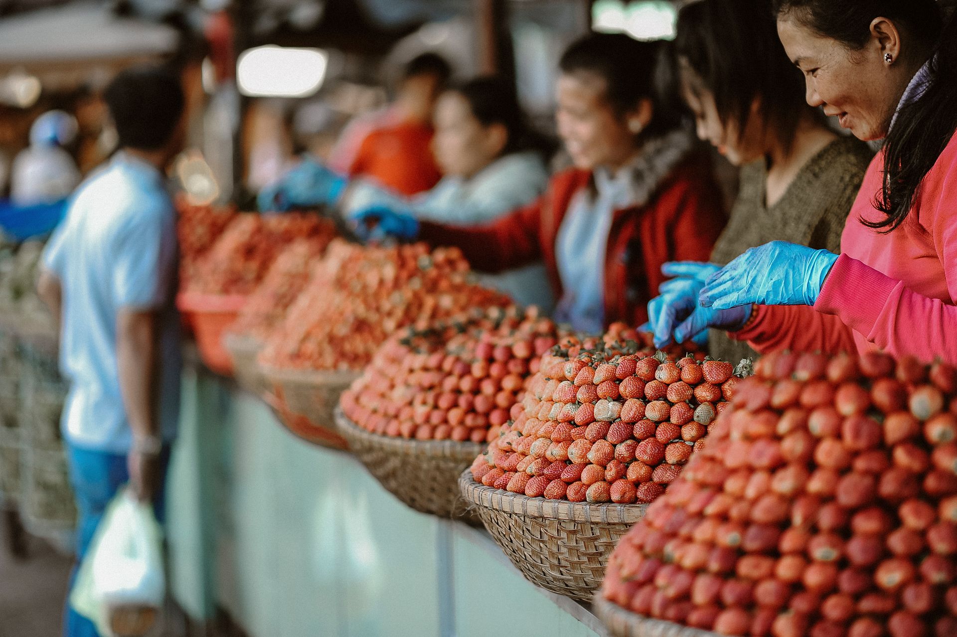Vibrant fruit market scene with women selling fresh strawberries in woven baskets outdoors.