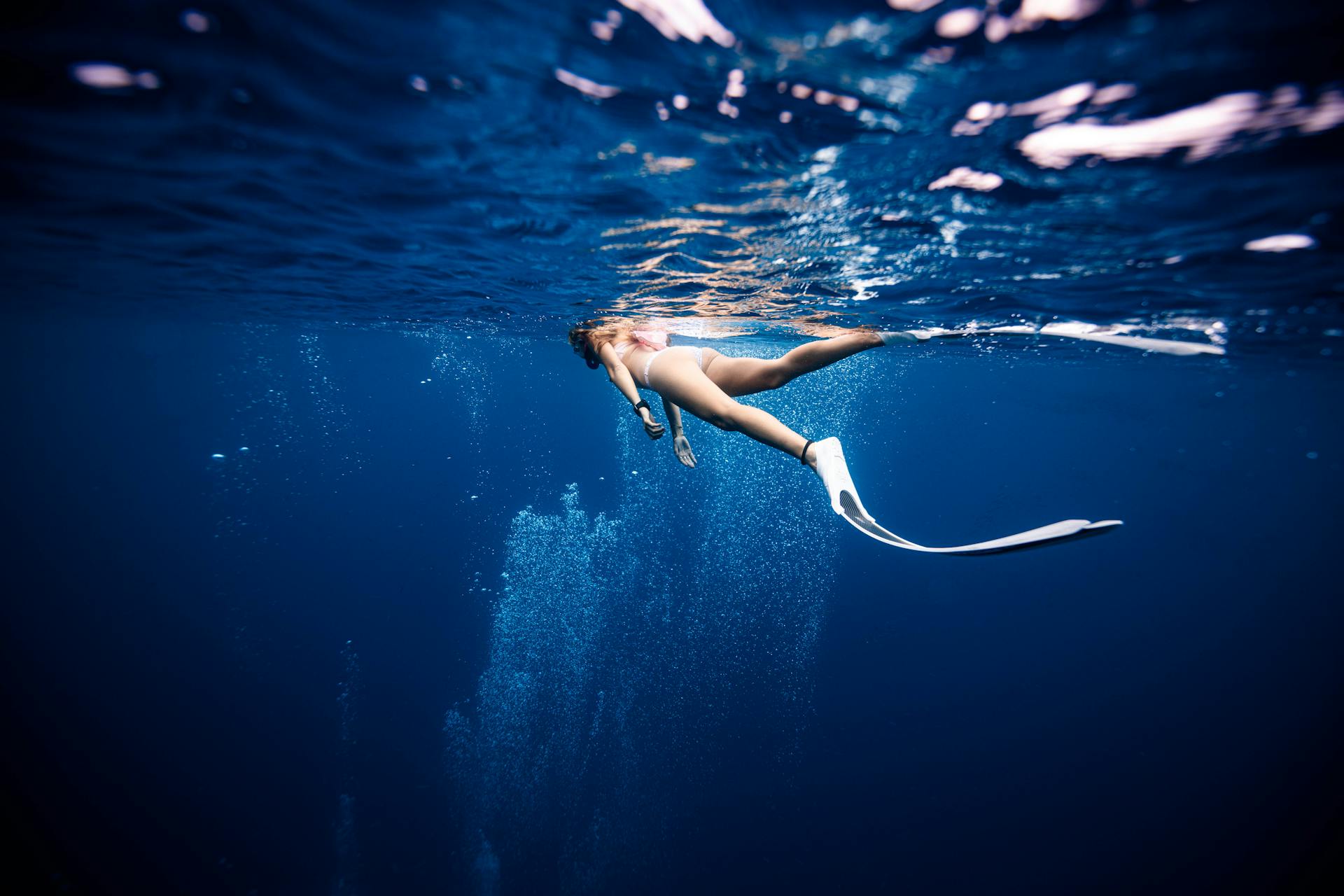 Female diver in swimwear and flippers swimming on surface of deep blue ocean