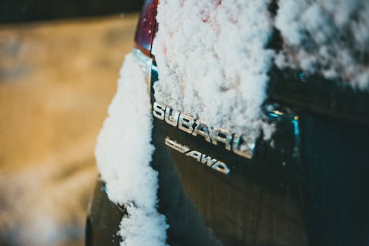 Close-up of a snow-covered Subaru emblem on a car in winter, highlighting the AWD feature.